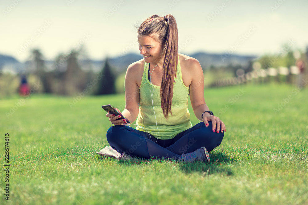 beautiful young sporty brunette relaxing in a park, stretching and looking at her phone beautiful young sporty brunette relaxing in a park, stretching and looking at her phone