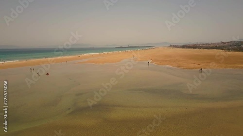 AERIAL ZOOMING OUT. People walking along beach and lagoon.
