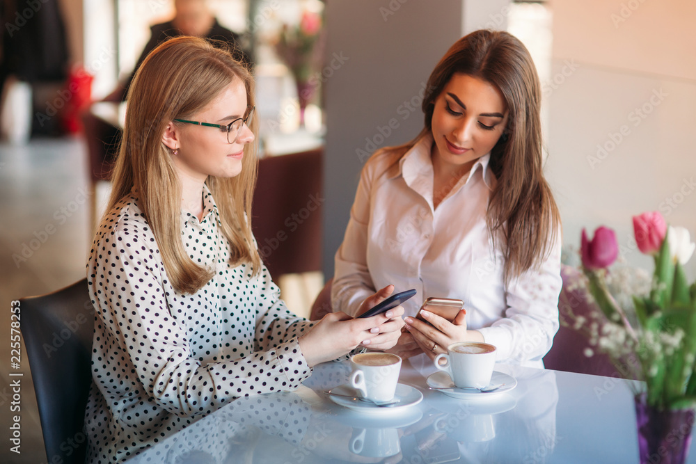 girls sitting in a cafe drinking cappuccino and using telephones girls sitting in a cafe drinking cappuccino and using telephones