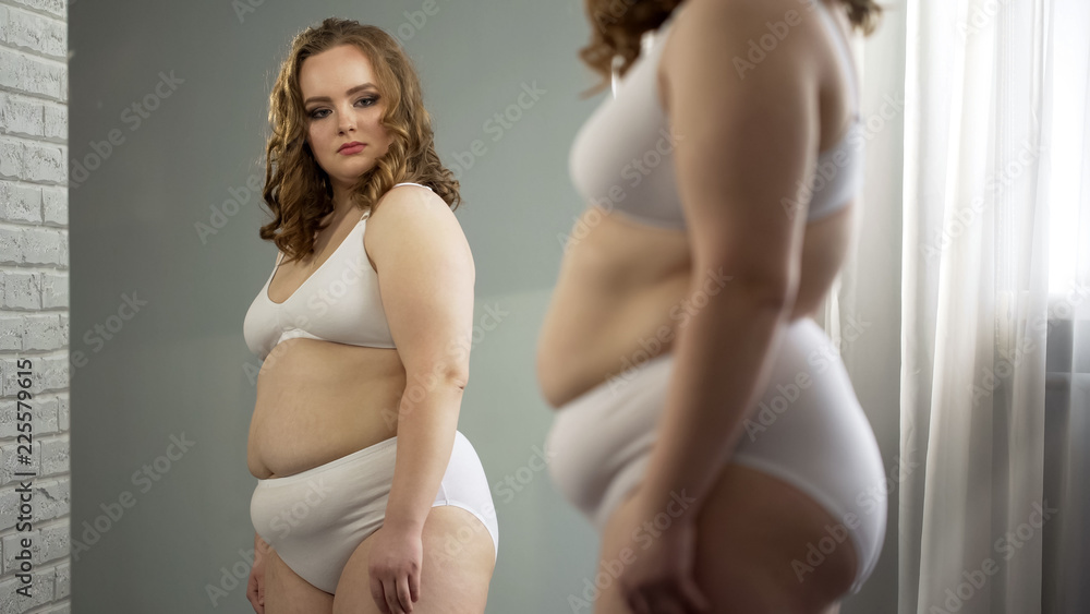 Fat lady attentively looking at her mirror reflection, accepting oversize  body Stock Photo