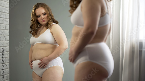 Fotografía Overweight female seriously looking at her mirror reflection, health problem