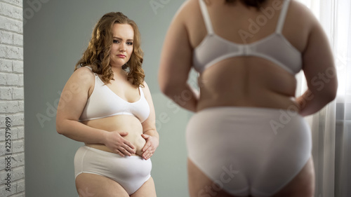 Depressed oversize woman in underwear looking in mirror, overweight problem