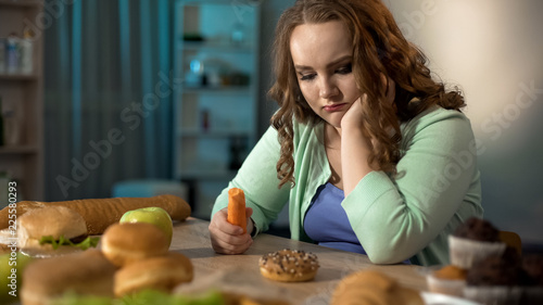 Sad fat girl eating carrot and dreaming about sweet donut  healthy dieting