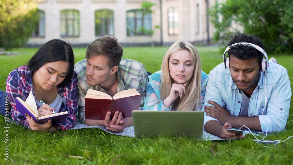 Group of friends lying on lawn on campus and preparing for test, student life