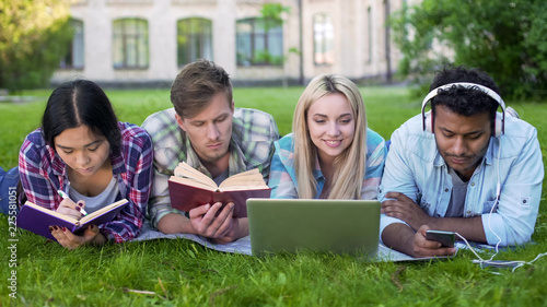 Multi-ethnic men and women doing homework on grass on campus, higher education