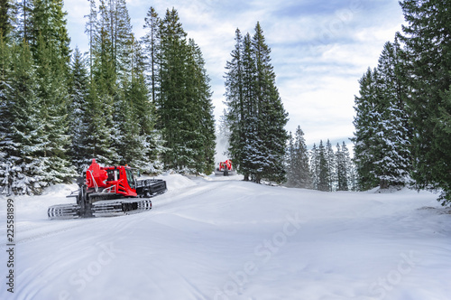 Snow groomers on alpine road through forest
