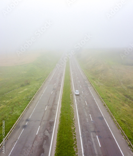 Aerial view of the road with a passing car and a field in the autumn, foggy morning. Photo from the drone