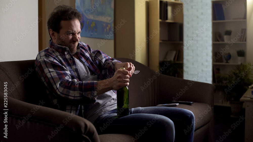Fototapeta premium Alcoholic opening beer bottle with fork, sitting alone on couch in dark room