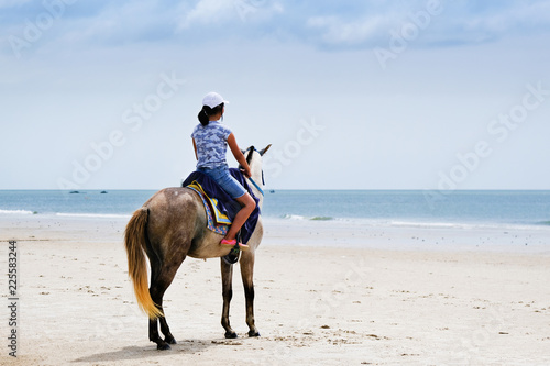 Back of young asian girl ridding horse on the beach.