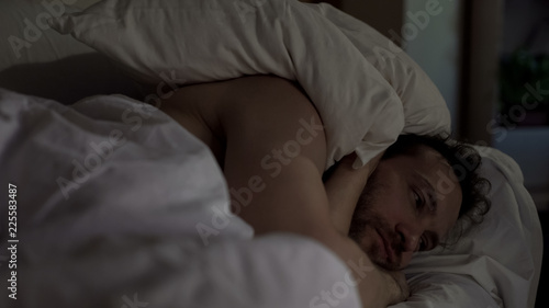 Tablou pe pânză Annoyed man tossing and turning in bed unable to fall asleep, noisy neighbors