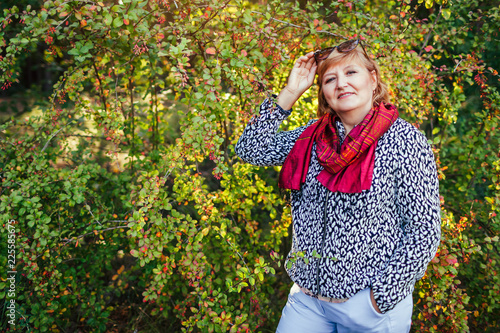 Stylish middle-aged woman posing in autumn forest. Senior lady wearing fall clothes and accessories