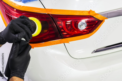 Car polish wax worker hands applying protective tape on the rearlights before polishing. Buffing and polishing car headlight. Car detailing photo