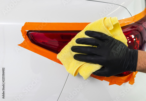 Car polish wax worker hands applying protective tape on the rearlights before polishing. Buffing and polishing car headlight. Car detailing photo