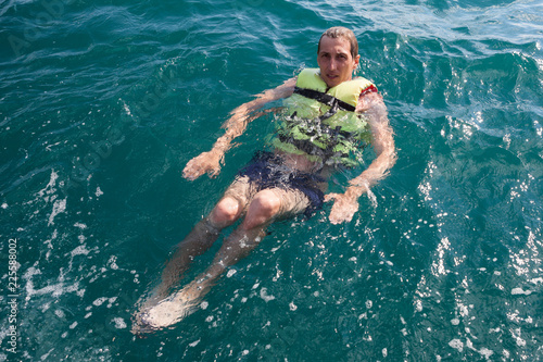 European young man staying afloat with cork lifesaving vest in open ocean