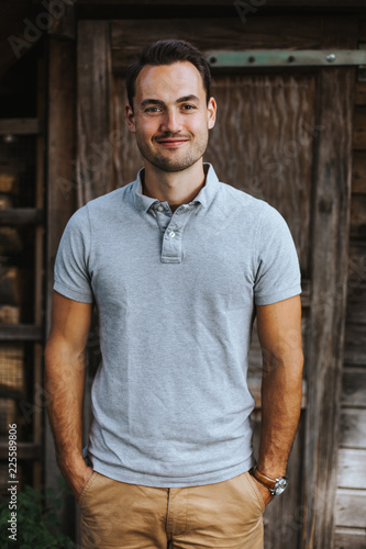 lächelnder dunkelhaariger Mann vor einer Holzhütte