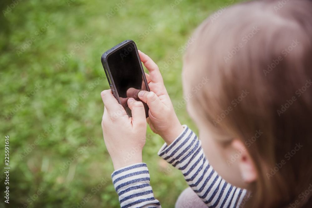 Cute little girl is using the smart phone. grass on background.