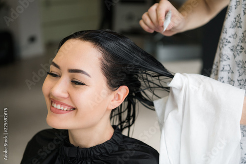 Hairdresser cutting woman's hair in salon, smiling, front view, close-up, portrait