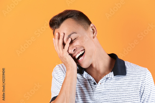 Portrait of handsome young man laughing on color background