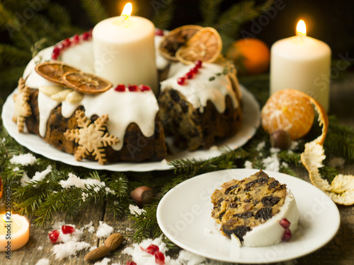 Christmas English fruitcake with candied fruit, dried fruit and nuts, decorated with white icing on a wooden background with fir branches, candles. Festive English cuisine