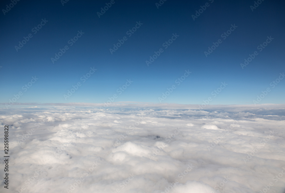 view from window of airplane, clouds below, blue sky, above the clouds