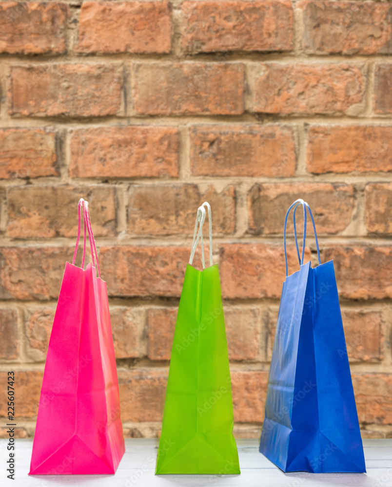 Three shopping bags on wooden table against brick wall