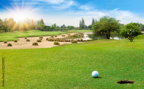 White Golf ball on green course near hole cup to be win on blurred beautiful landscape of golf course in bright day time with copy space. Sport  Recreation  Relax in holiday concept