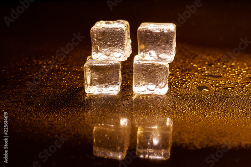 Golden ice cubes reflection on black table.