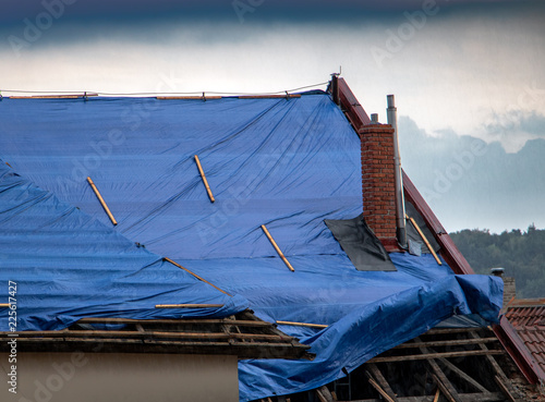 The protective tarpaulin on the roof flutters at the storm with rain. The tarp covers the roof of the old house in the reconstruction.