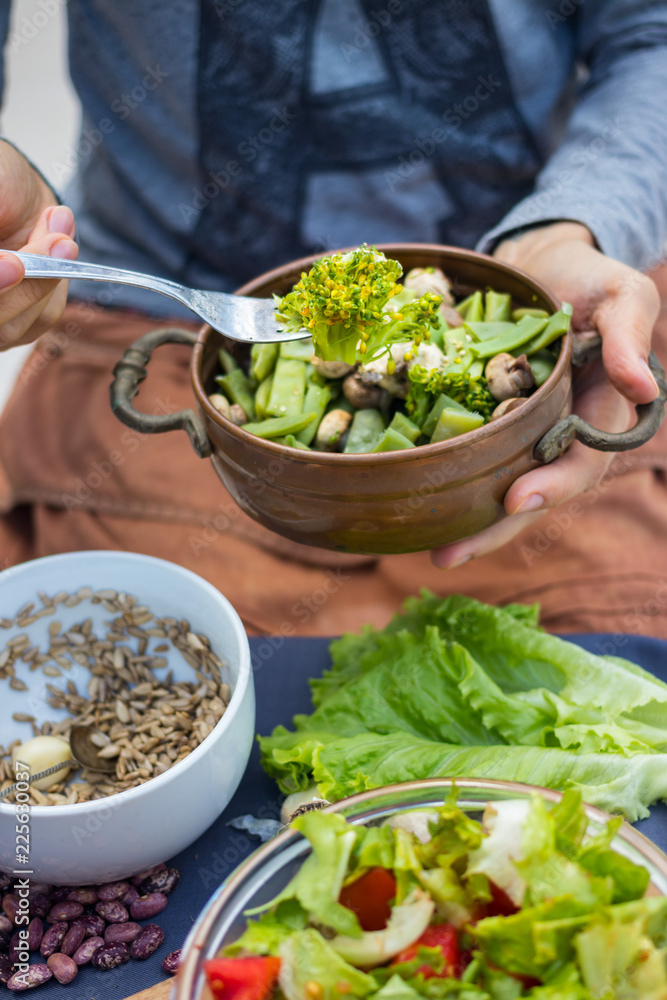 Woman hands hold a copper pot with cooked green beans, broccoli and mushrooms vegetables. Vegan vegetarian healthy food. Lunch or dinner. Woman hands hold a copper pot with cooked green beans, broccoli and mushrooms vegetables. Vegan vegetarian healthy food. Lunch or dinner.