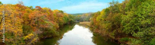 Panorama of the autumn forest along the banks of the river. Colorful autumn trees along the banks of the river. Panorama of forest and river in the autumn season.