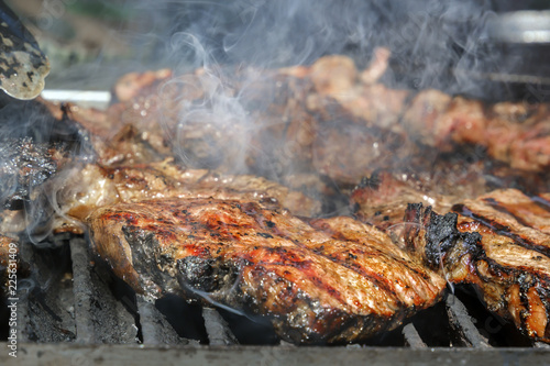 Meat steaks are cooked on a hot grill with smoke. Close-up