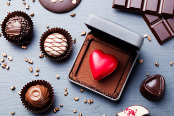 Heart shaped chocolate candy in a gift box on slate background. Top view.