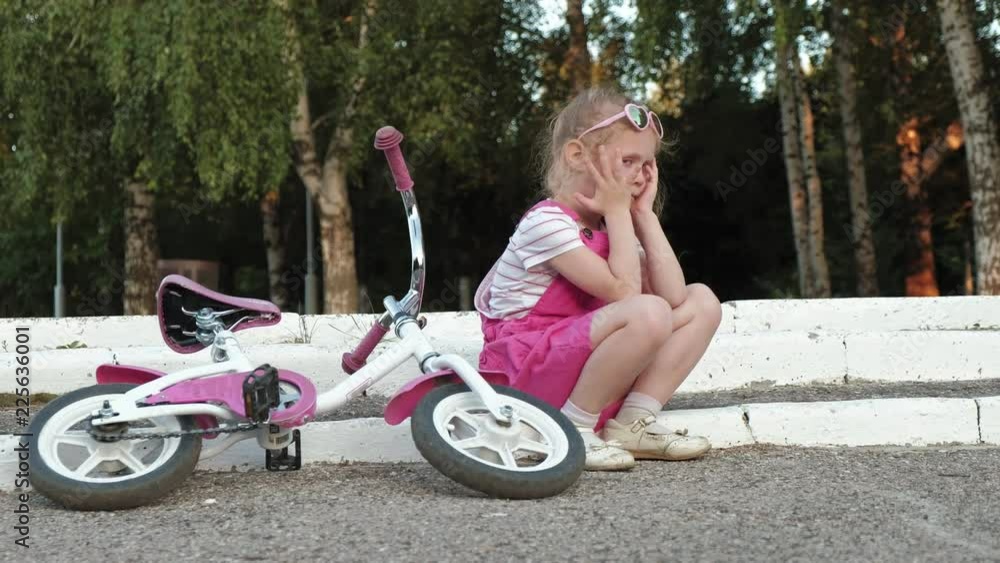 A little beautiful girl in a pink dress is sitting in the park on the ...