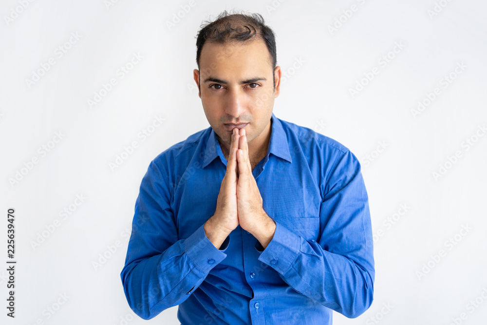 Portrait of serious businessman praying and looking at camera. Indian manager standing with pensive expression. Hope concept Portrait of serious businessman praying and looking at camera. Indian manager standing with pensive expression. Hope concept