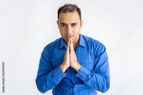 Portrait of serious businessman praying and looking at camera. Indian manager standing with pensive expression. Hope concept