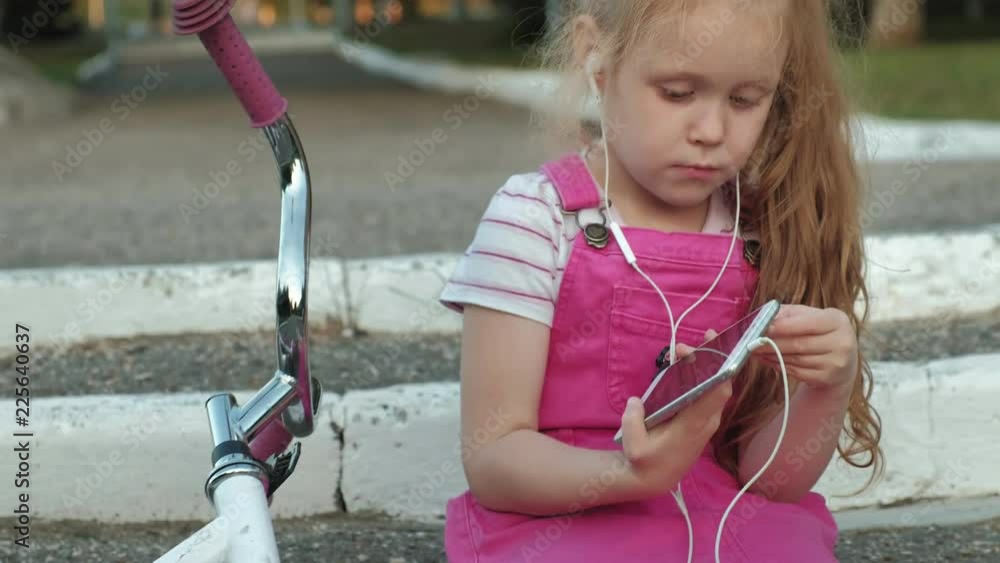 A little beautiful girl in a pink dress is sitting in the park on the ...