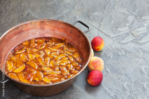 Fresh bright peaches and nectarins lay on the stone bricks, close to the copper jar, full of peach jam. Close up, outdoor, copy space. photo