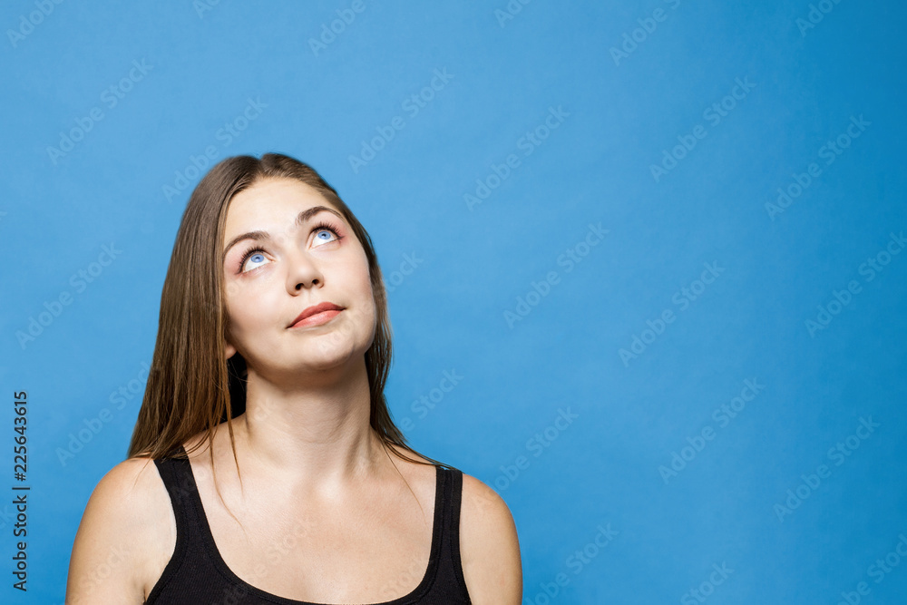 Young causacian woman with blue eyes up thinks or dreams about something. Dark hair, isolated on blue background, studio, model, copy space. Young causacian woman with blue eyes up thinks or dreams about something. Dark hair, isolated on blue background, studio, model, copy space.