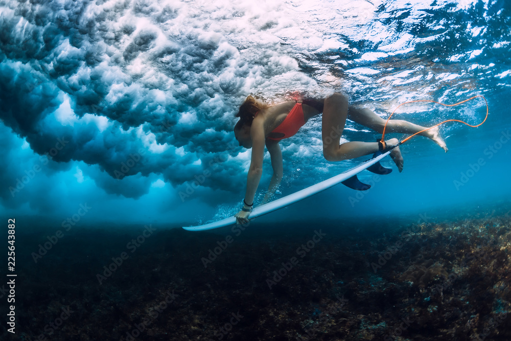 Professional surfer woman with surfboard make duck dive underwater with ocean wave.