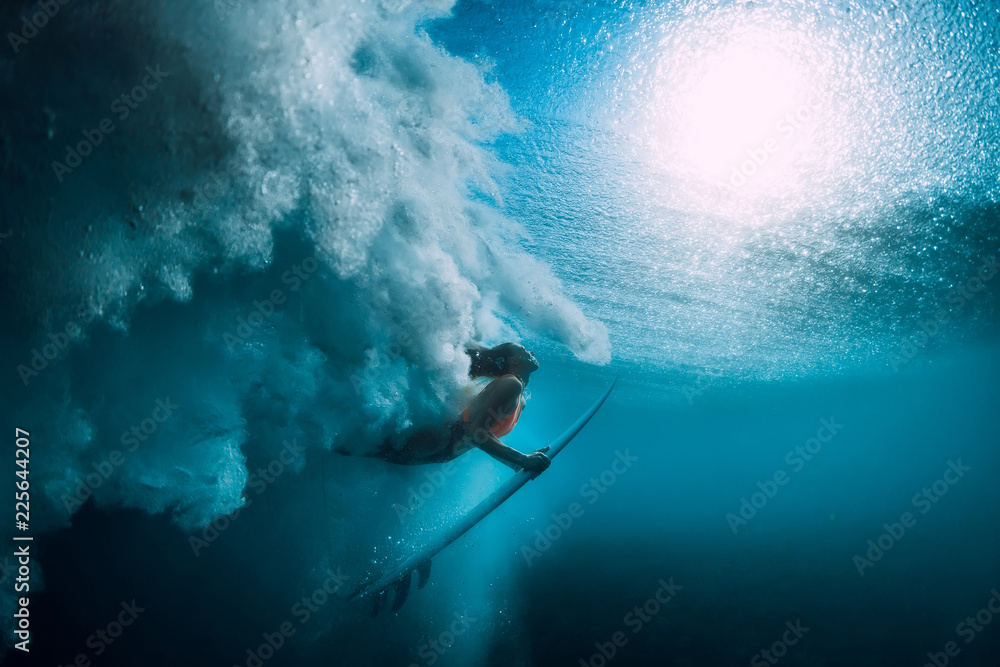 Fototapeta Surferka z deską surfingową nurkować pod wodą z dużą falą oceanu.