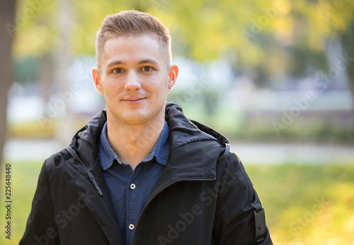 Handsome and young man in a black jacket standing in the park. Portrait photo