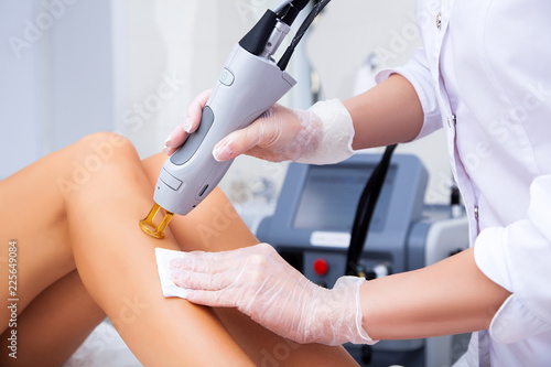 Close-up of a female cosmetologist in a medical coat making a young woman  a procedure laser hair removal for leg. Cosmetology, ionization, diamond procedures.