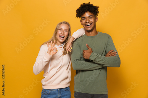 Photo of cheerful students man and woman 16-18 with dental braces laughing and gesturing at camera, isolated over yellow background photo