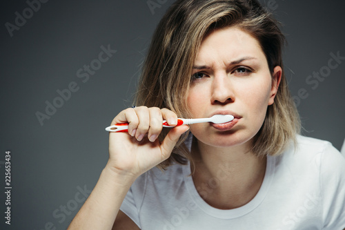 Young woman brushing her teeth. Her face is sullen and sleepy.
