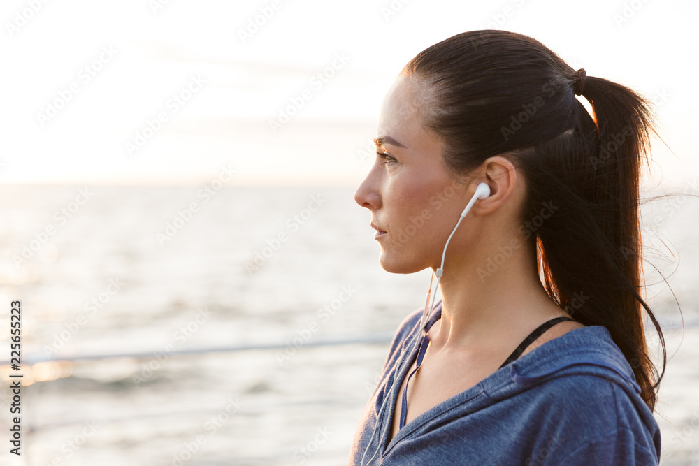 Serious young sports woman outdoors on the beach listening music with earphones. Serious young sports woman outdoors on the beach listening music with earphones.