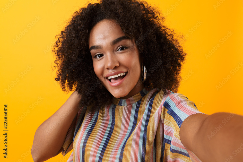Beautiful young happy african cute girl posing isolated over yellow background take a selfie. Beautiful young happy african cute girl posing isolated over yellow background take a selfie.