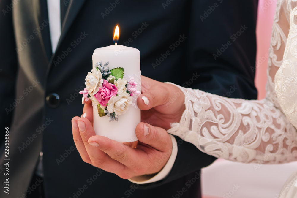 White candle with a decoration of flowers in the hands of the newlyweds. The concept of the family hearth
