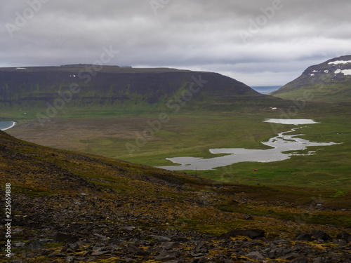 Northern summer landscape, beautiful snow covered cliffs and fljotsvatn lake in Fljotavik cove in Hornstrandir, west fjords, Iceland, with river stream, green grass meadow, moody sky photo