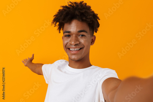 Happy young african man posing isolated over yellow background showing copyspace make se;fie by camera.