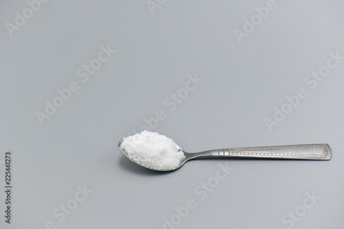 Spoon filled with sea salt on gray background.